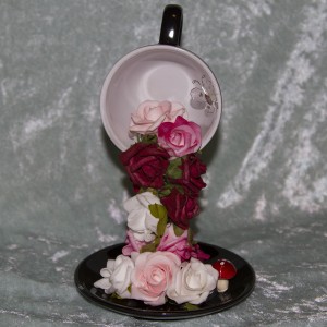 Black cup and saucer with cascading white, pink and burgundy roses. Trimmed with a white butterfly and toadstool. $25